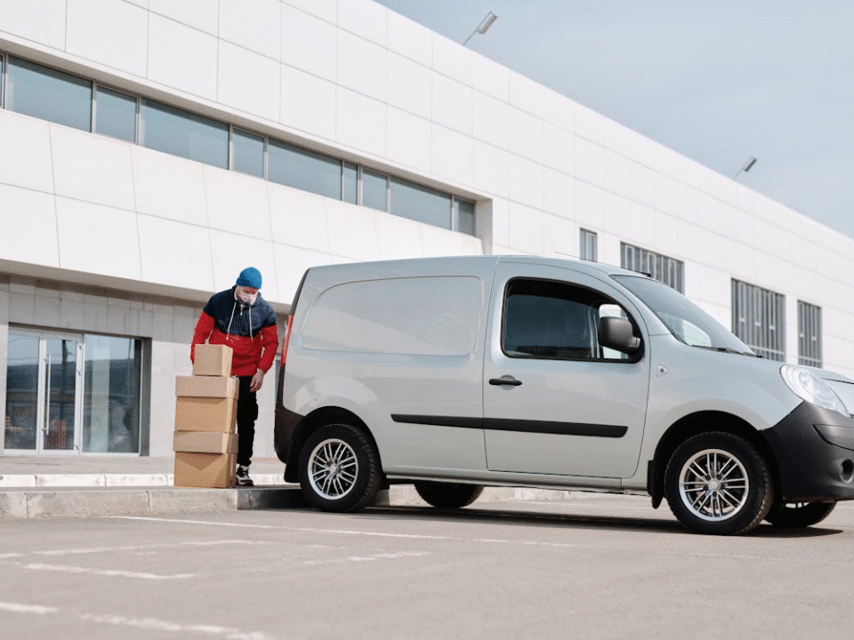 Courier in front of his van loading packages with a warehouse in the background.